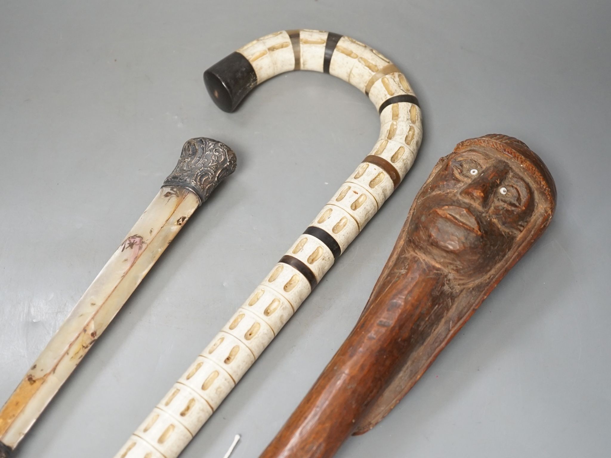 A carved wood figural walking cane, a vertebrae walking stick and a Victorian parasol. Longest 108cm